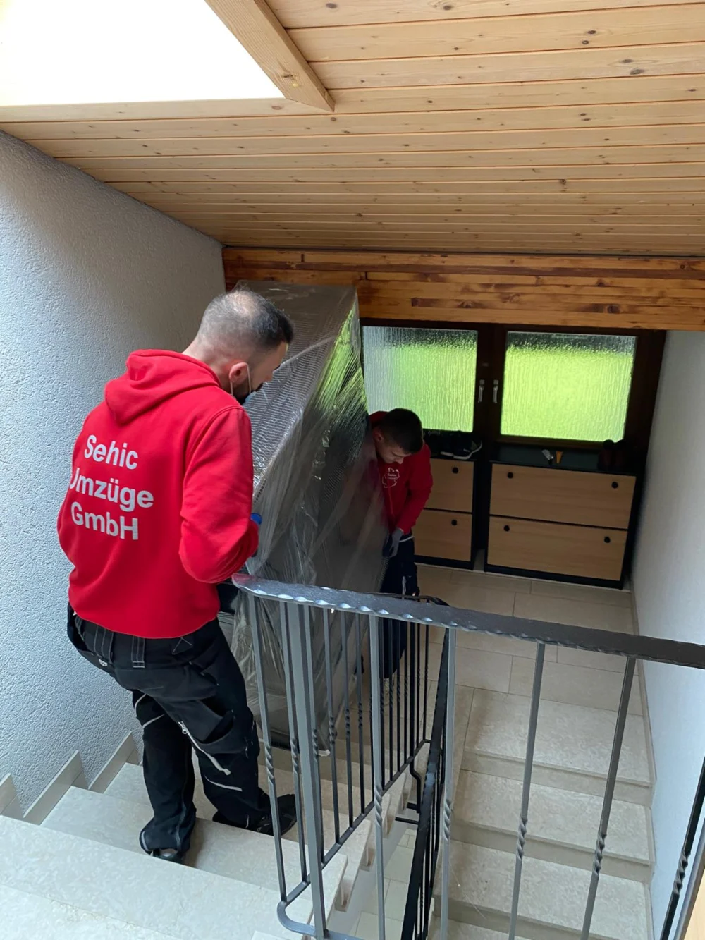 Möbelpacker von Sehic Umzüge tragen ein eingepacktes Möbelstück für den Fernumzug aus dem Haus