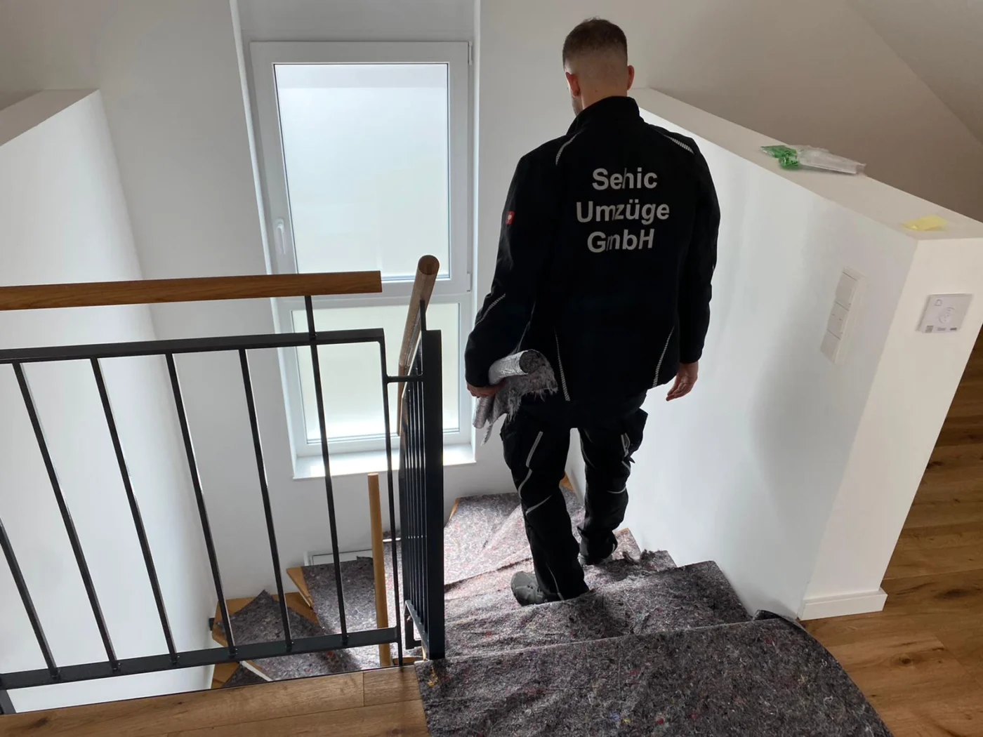 Möbelpacker von Sehic Umzüge trägt beim Privatumzug in Karlsruhe ein eingepacktes Möbelstück durchs Treppenhaus