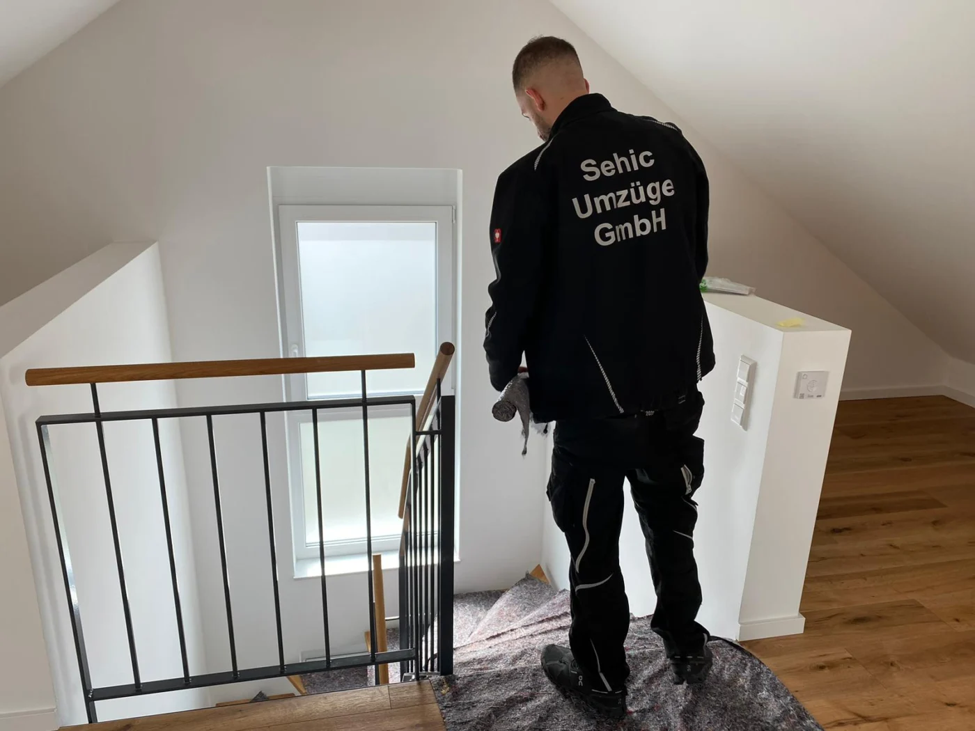Möbelpacker von Sehic Umzüge trägt ein Gerät über die mit Bodenschutz ausgelegte Treppe beim Seniorenumzug in Karlsruhe
