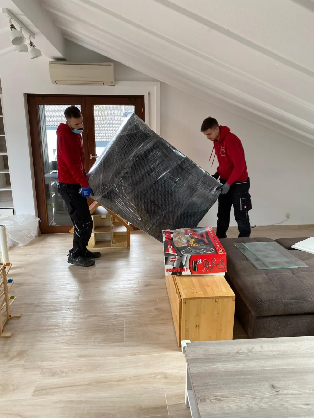 Zwei Möbelpacker von Sehic Umzüge tragen beim Seniorenumzug in Karlsruhe ein eingepacktes Sofa aus der Wohnung